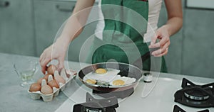 Chef in a green apron cooking four eggs in a pan, the background looking aesthetic.