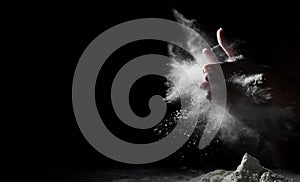Chef hand clap with splash of white flour and black background with copy space.