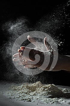 Chef hand clap with splash of white flour and black background with copy space.