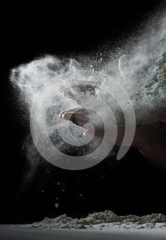 Chef hand clap with splash of white flour and black background with copy space.