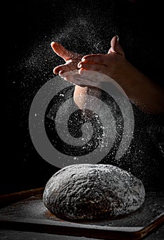 Chef hand clap with splash of white flour and black background with copy space. woman`s hands Making bread