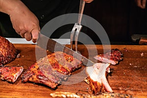 Chef hand cutting grilled ribs by sharp knife and fork