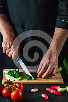 Chef is hands close-up cuts young green onions on a restaurant kitchen cutting board for salad. Vegetable diet or snack idea