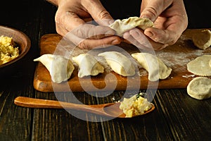 Chef hands close-up making dumplings from dough. The concept of cooking dumplings with potatoes on the kitchen table in a