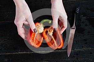Chef hands cut red bell pepper on black wooden background.