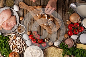 Chef hands cuts with knife mushrooms on wooden chopped board with variety of ingredients background. Concept of cooking process.