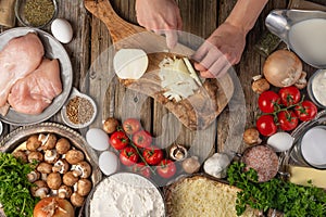 Chef hands cuts with knife onion on wooden chopped board with variety of ingredients background. Concept of cooking process.