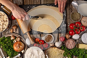 Chef hands cuts with knife-wheel the dough for pie on wooden table with variety of ingredients background. Concept of cooking