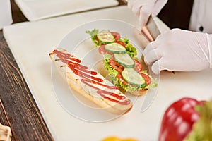 Chef hands cutting sausage to hot dog.