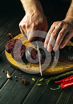 Chef hands with a knife cut blood sausage on a kitchen cutting board. Cooking a national dish with spices and pepper at home in