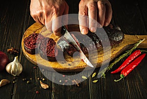 Chef hands with a knife cut blood sausage on a kitchen cutting board. Cooking a national dish with spices and pepper at home in