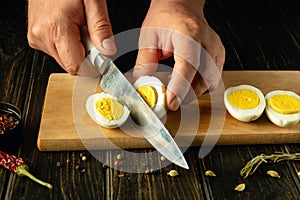 Chef hands and knife cutting a boiled egg in the kitchen for cooking or catering food. Gourmet meal concept on kitchen table in