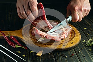 Chef hands with a knife cutting meat on a kitchen cutting board. Low key concept of preparing a meat dish for lunch