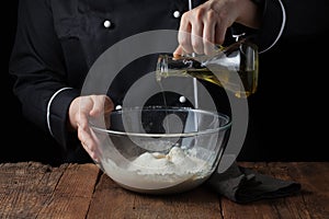 Chef hands pours olive oil in bowl on raw dough on a black background, Cooking process dough for pizza