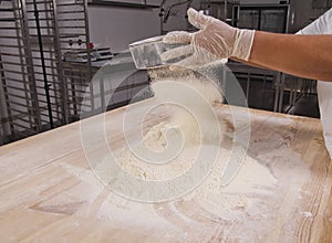 Chef hands sifting flour on wooden tabletop