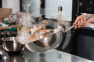 Chef hands toss food at kitchen. Closeup chef hands with wok cook food.