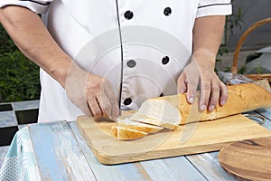 Chef holding knife cutting slide bread making on wooden board