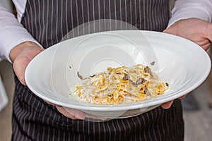 Chef holding a plate of spaghetti with mushrooms, close-up