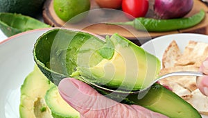 Chef holds half of a pitted avocado in his hand and scoops it out from the skin with a spoon