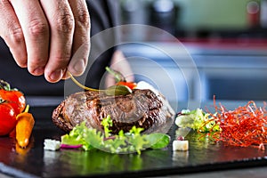 Chef in hotel or restaurant kitchen cooking, only hands. Prepared beef steak with vegetable decoration