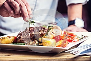 Chef in hotel or restaurant kitchen cooking only hands. Prepared beef steak with vegetable decoration