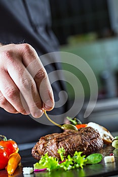 Chef in hotel or restaurant kitchen cooking, only hands. Prepared beef steak with vegetable decoration