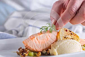 Chef in hotel or restaurant kitchen cooking, only hands. Prepared salmon steak with dill decoration