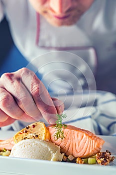 Chef in hotel or restaurant kitchen cooking, only hands. Prepared salmon steak with dill decoration