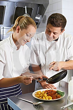 Chef Instructing Trainee In Restaurant Kitchen