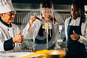 Chef instructs in kitchen. Schoolgirls make Japanese noodle. Kids and teacher at