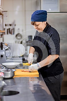 The chef in the kitchen cuts a tomato and prepares a Greek salad. Concept of Ñooking vegetarian salad