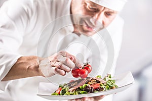 Chef in the kitchen of the hotel or restaurant decorates the food just before serving photo