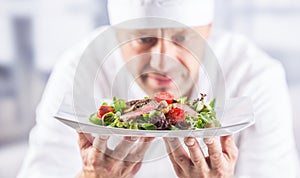 Chef in the kitchen of the hotel or restaurant holding plate with food before serving