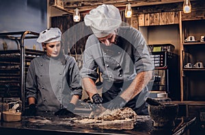 Chef kneading dough in the kitchen. Chef teaching his assistant to bake the bread in the bakery.