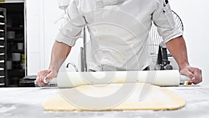 Chef kneading dough with rolling pin at commercial kitchen. Pastry Chef kneading dough on the table at pastry shop.