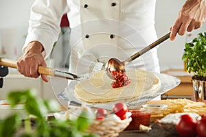 Chef ladling tomato paste onto a pizza base