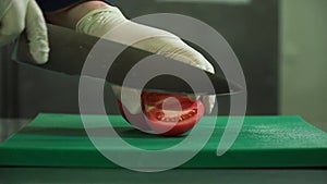 A chef with a large knife cuts a tomato. Cooking in the restaurant. Close-up