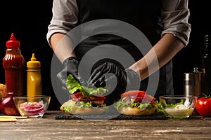 The chef lays out a fresh salad on a burger, with ingredients in the background. Horizontal photo, Tasty and unhealthy food, fast