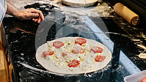 Chef making Caprese Bianca Pizza by adding olive oil on dough with sliced tomato, mozzarella and parmesan cheese before baking