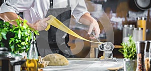 Chef making spaghetti noodles with pasta machine on kitchen table with some ingredients around