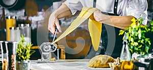 Chef making spaghetti noodles with pasta machine on kitchen table with some ingredients around