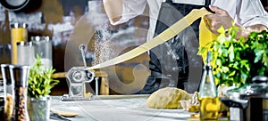 Chef making spaghetti noodles with pasta machine on kitchen table with some ingredients around