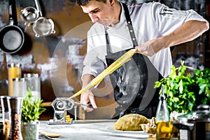 Chef making spaghetti noodles with pasta machine on kitchen table with some ingredients around