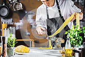 Chef making spaghetti noodles with pasta machine on kitchen table with some ingredients around