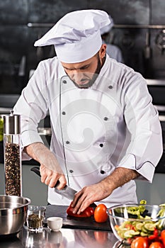 Chef male with knife at restaurant kitchen. Professional chef cutting tomato.