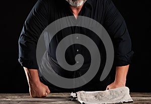 Chef man in black uniform bent over a wooden table and rested his fists