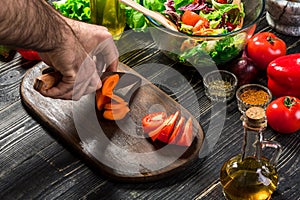 Chef man cooking in the kitchen. Man`s hand cuts carrot on a wooden board