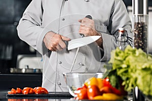 Chef man sharpen knife at kitchen restaurant. Male professional sharpen knife.