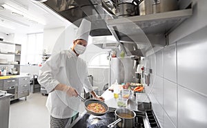 Chef in mask cooking food at restaurant kitchen