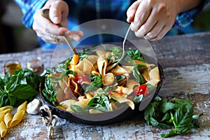 Chef mixes pasta with basil and spices in a pan. Appetizing pasta in a pan with tomatoes, basil and spices. One pan pasta. Italian